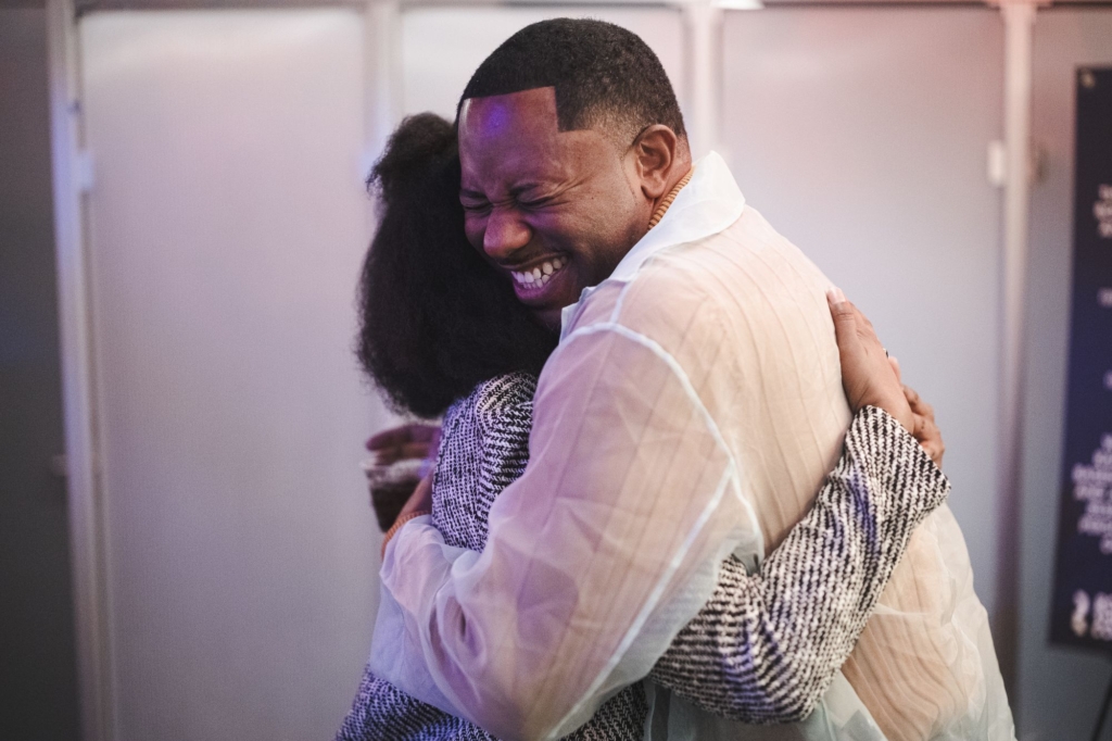 A man squishes his face in a huge smile while hugging a woman at an event.